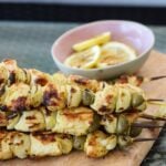 Poulet Yassa Skewers on a wooden board with lemon wedges.