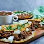 Birria Quesadillas on a wooden board with other edibles around it.