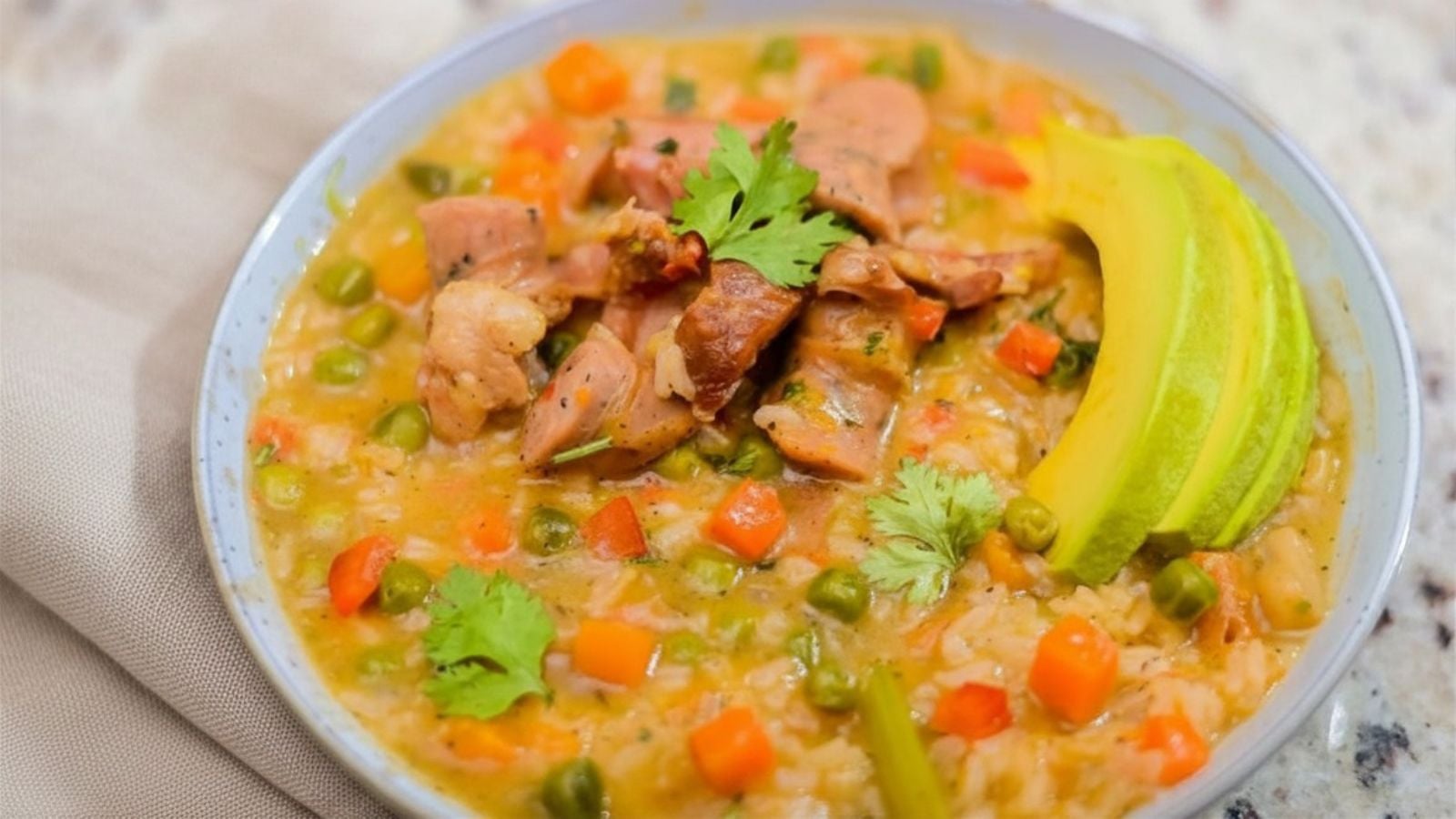Dominican longaniza asopao served in a bowl with rice, vegetables, sausage, cilantro, and avocado.