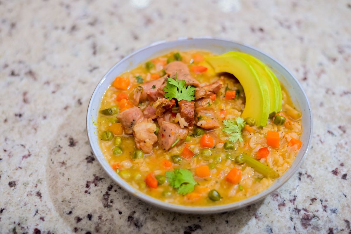 Pot of Dominican rice asopao with longaniza, peas, carrots, herbs, and creamy seasoned broth.