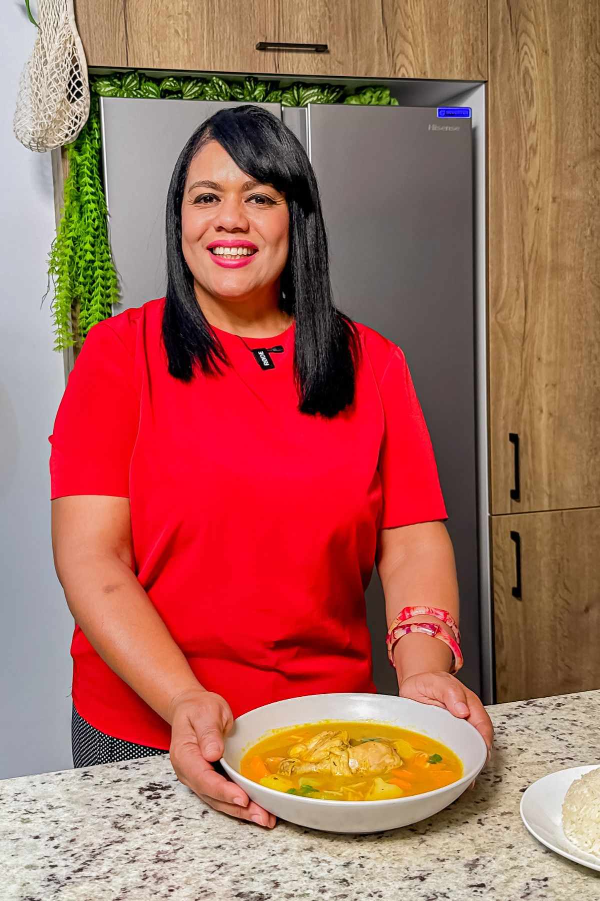 Woman in a red shirt holding a bowl of Dominican chicken soup, with white rice on the side.