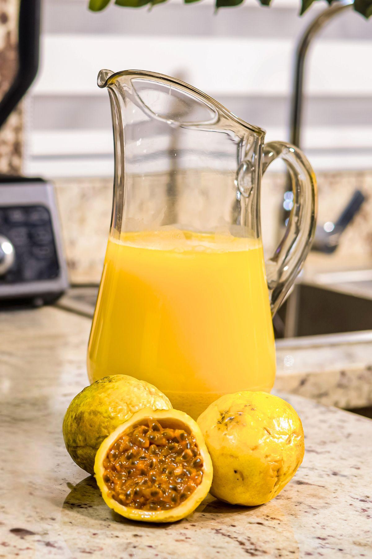A pitcher of passion fruit juice with oats beside fresh passion fruits on a kitchen counter.