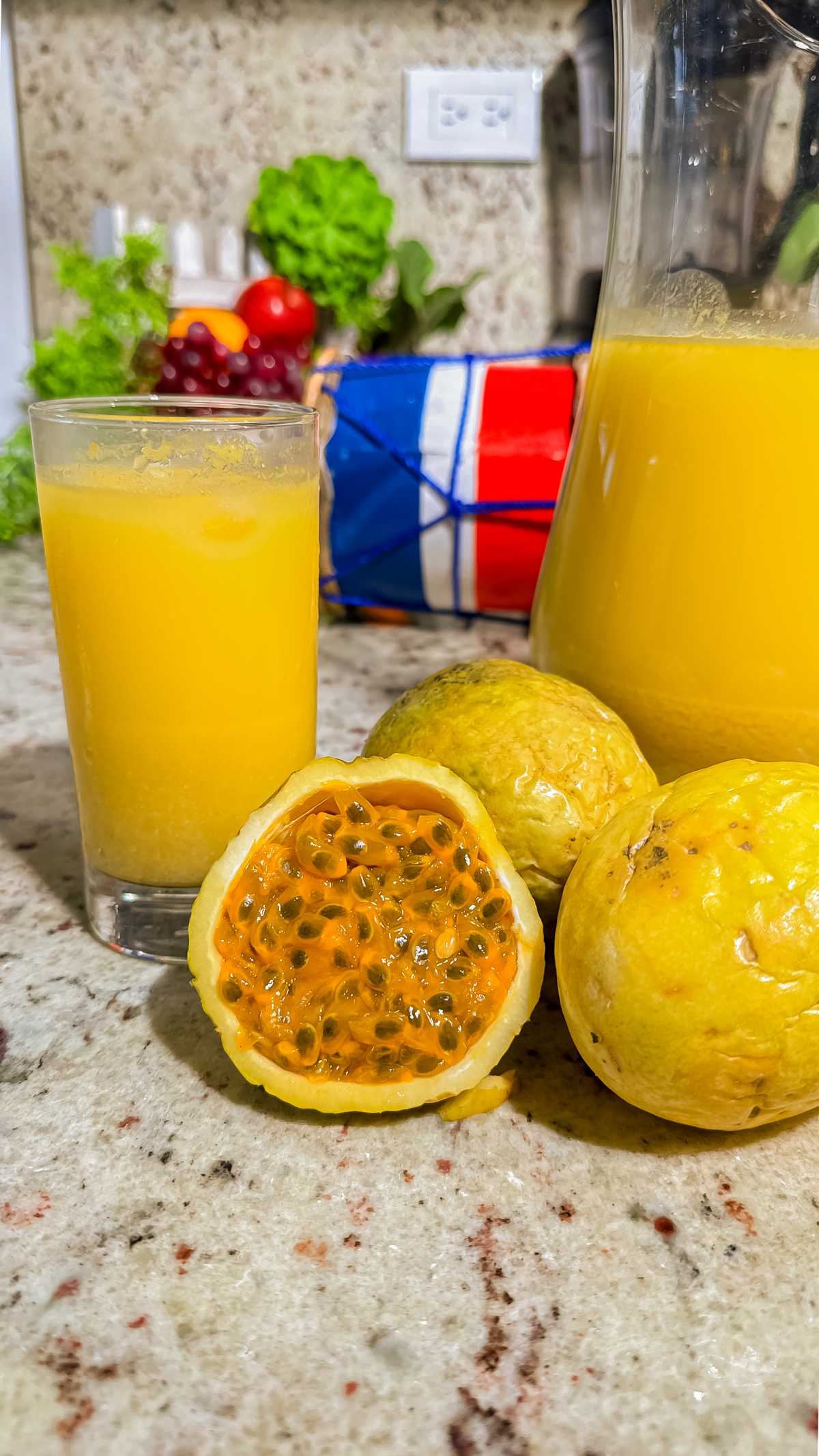 A glass and pitcher of passion fruit juice with oats beside fresh passion fruits on a kitchen counter.