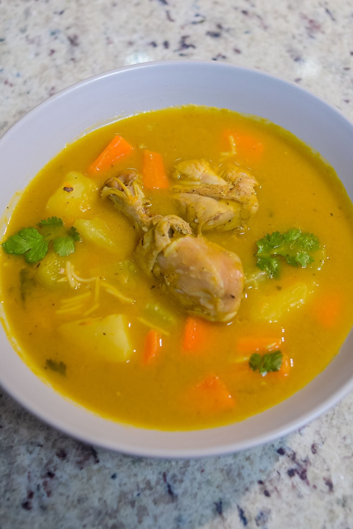 Bowl of Dominican chicken soup with chicken, potatoes, carrots, and cilantro in a golden broth.