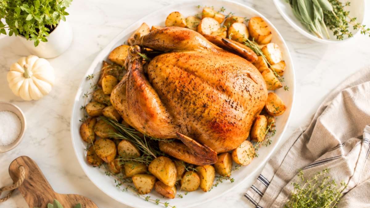 Golden roasted turkey with potatoes, rosemary, and thyme on a serving platter